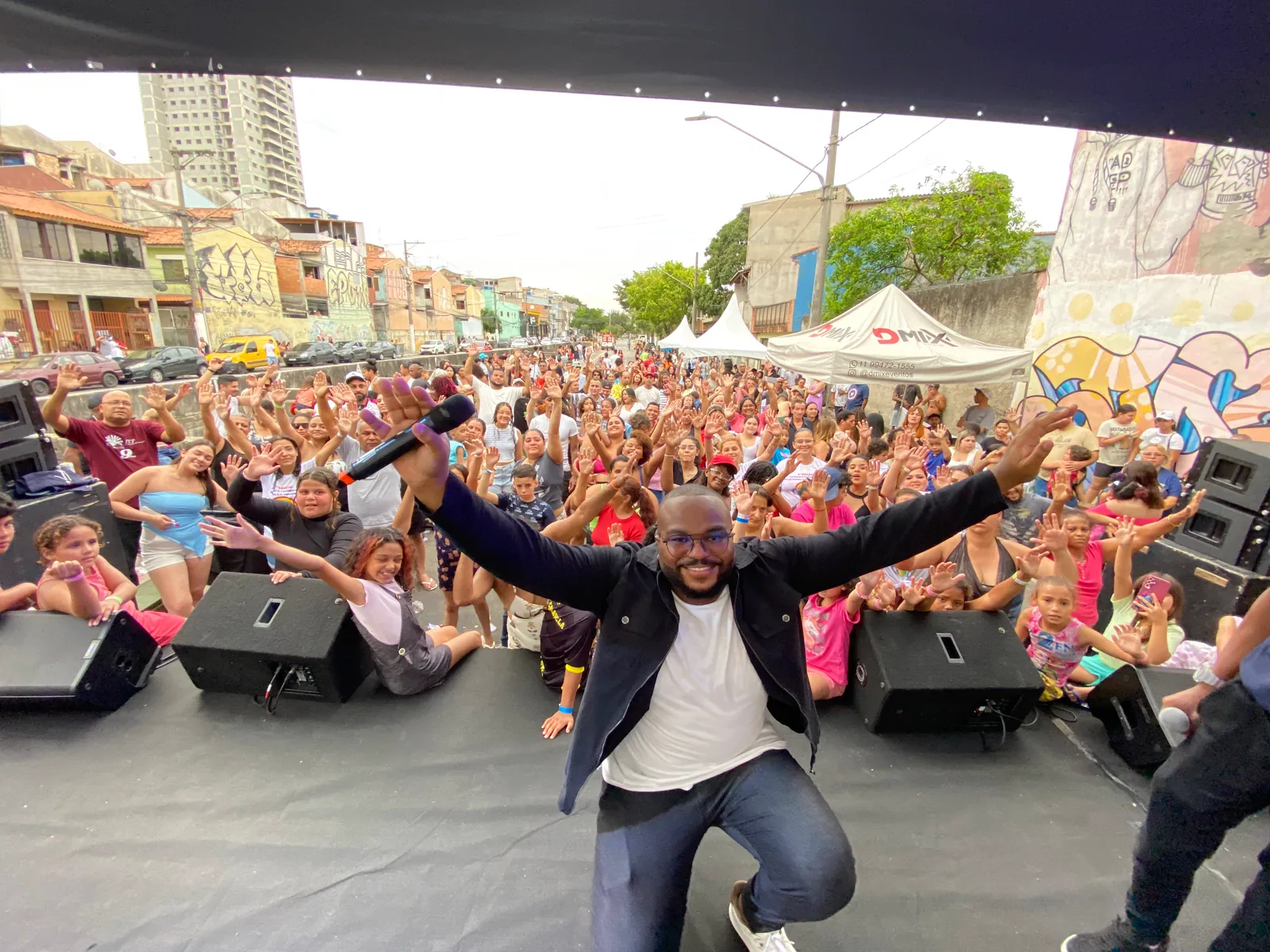 Kelvim agachado na beira do palco, com o público ao fundo, em evento ao ar livre